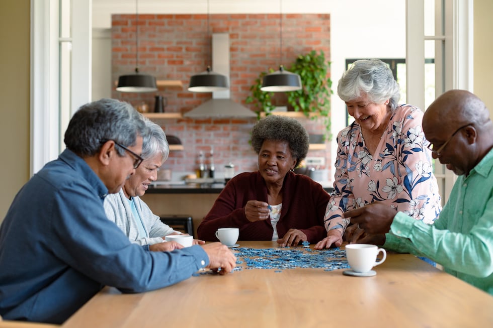 Group of diverse senior male and female friends doing puzzles at home. socializing with...