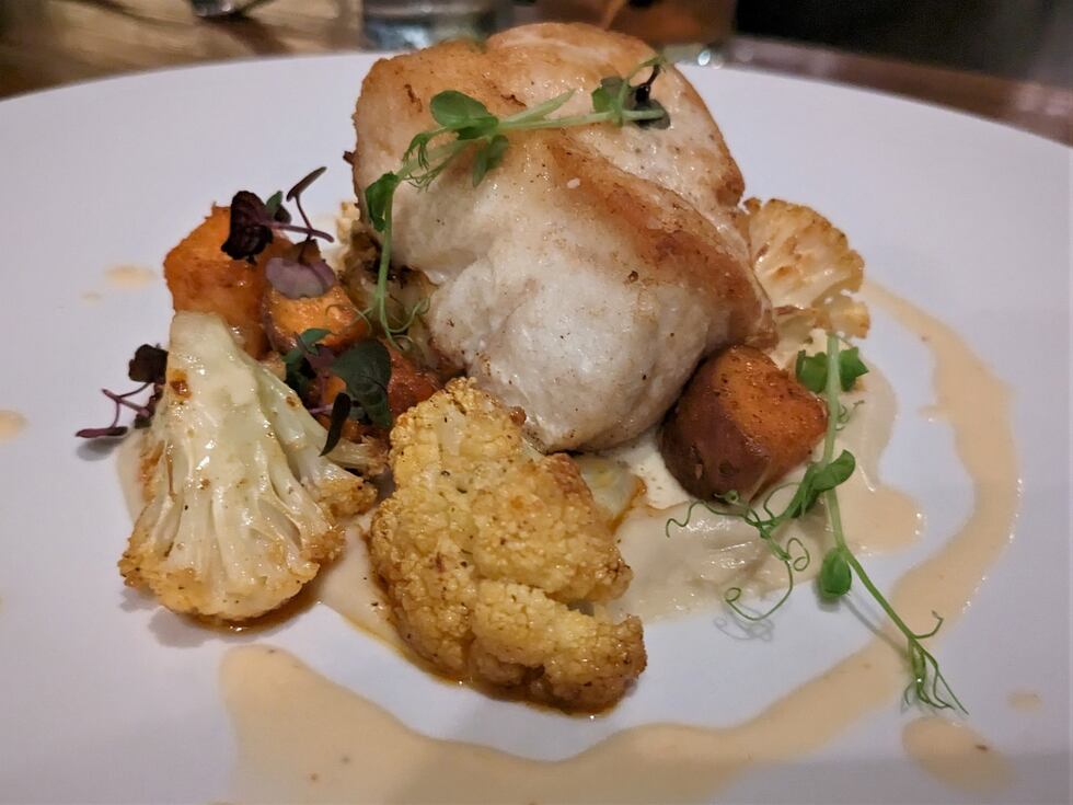A delicate cut of fish, rests on a bed of pureed root vegetables, roasted cauliflower, and...